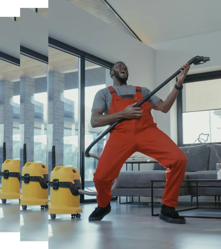 A fun image of cleaner wearing orange overalls happily holding a hover whilst cleaning a house